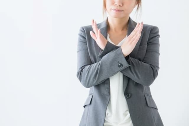 手で×をつくっている女性